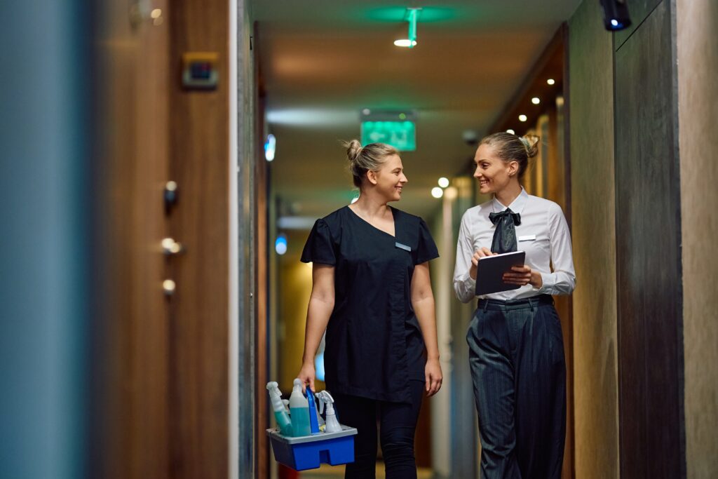 Happy,Housekeeping,Executive,Using,Touchpad,While,Communicating,With,Chambermaid,In